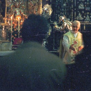 Here's a brief summary of the image: Priest performing a religious ritual, partially visible in darkness.