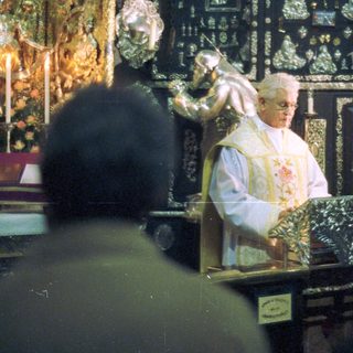 Priest officiating in an ornate, dimly lit church setting.