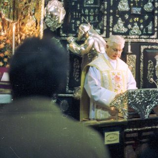 Priest performing a ceremony in an ornate, dark setting.