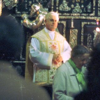 Priest performing a service with ornate religious backdrop.