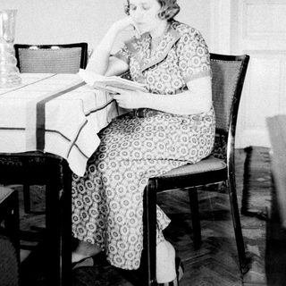 Woman sits reading at a table in a room.