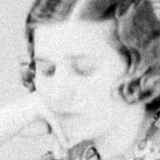 Woman sits reading at a table in a room.