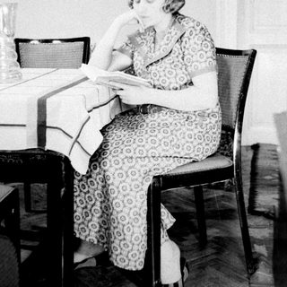 Woman sits reading at a table in a room.