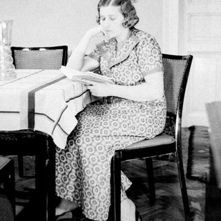 Woman sits reading at a table in a room.