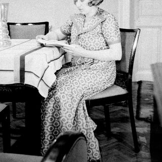 Woman seated at table, reading in a vintage-style room.