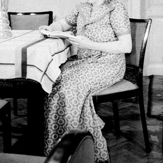 Woman seated at table, reading in a vintage-style room.
