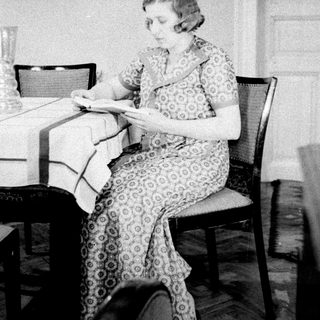 Woman seated at table, reading in a vintage-style room.