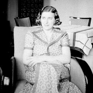 Woman in patterned dress seated in a vintage armchair.