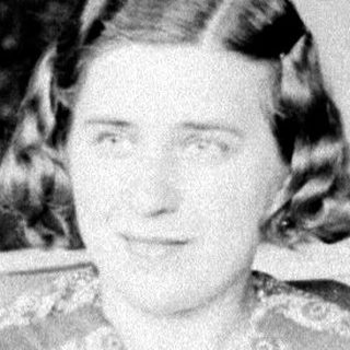 Woman in patterned dress seated in a vintage armchair.