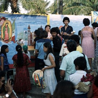 Group of people gathered before a religious mural outdoors.