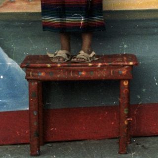 Girl in traditional dress stands before painted backdrop, being photographed.