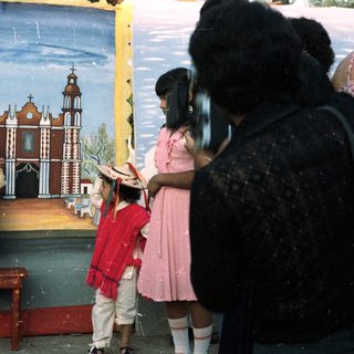 Girl in traditional dress stands before painted backdrop, being photographed.