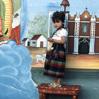 Girl stands on table before a mural, likely religious.