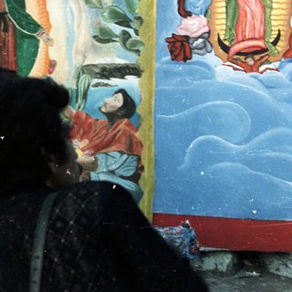 Girl stands on table before a mural, likely religious.