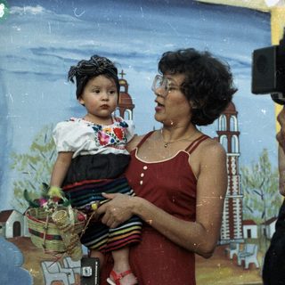 Woman holds child, being photographed in front of backdrop.