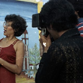 Woman holds child, being photographed in front of backdrop.