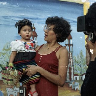 Woman holds child, being photographed in front of backdrop.
