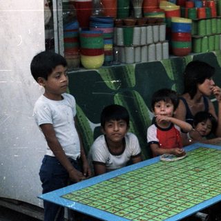 Children stand near a vendor's stall with colorful wares.