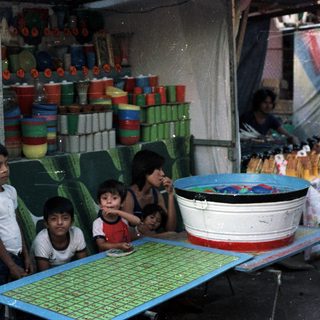 Children stand near a vendor's stall with colorful wares.