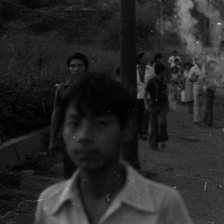 Crowd gathers on a road with vehicles and smoke.