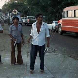 Four men stand on a road, near vehicles.