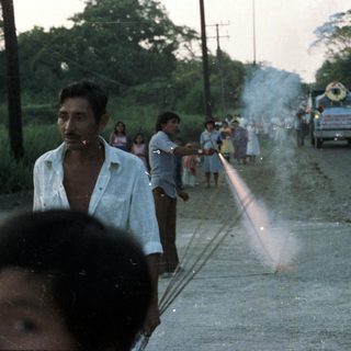 Man lighting fireworks on a road with onlookers.