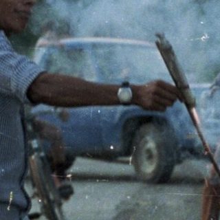 Man sparks fireworks on a road with onlookers.