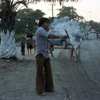 Man sparks fireworks on a road with onlookers.
