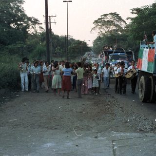 Parade or procession with trucks, people, and festive decorations.