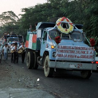 Parade or procession with trucks, people, and festive decorations.