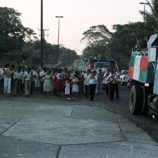 Procession with a truck, band, and crowd in a street.