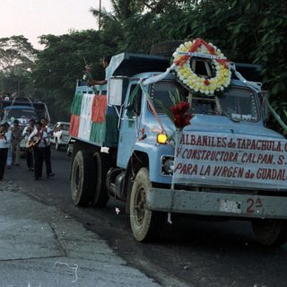 Procession with a truck, band, and crowd in a street.