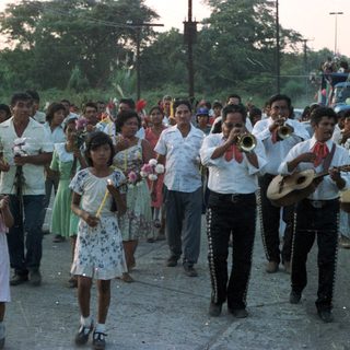 Procession with musicians and candle-bearers in a tropical setting.