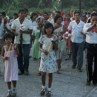 Procession with musicians and candle-bearers in a tropical setting.