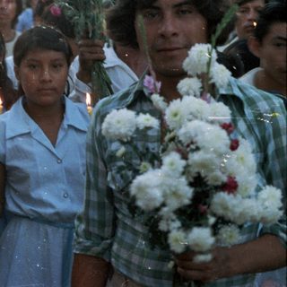 Group of people holding candles and flowers in a procession.