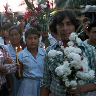 Group of people holding candles and flowers in a procession.
