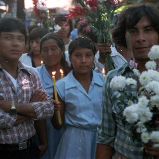 Group of people holding candles and flowers in a procession.