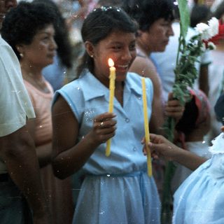 Girl holds candles, a child looks on in a crowd.
