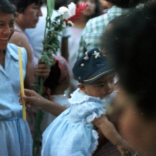 Girl holds candles, a child looks on in a crowd.