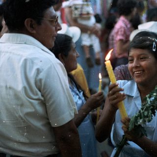 People hold candles, smiling, in a crowd scene.