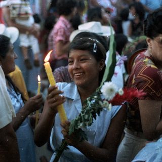 People hold candles, smiling, in a crowd scene.