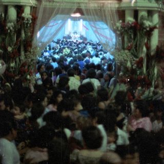 Crowded gathering in front of a decorated building or altar.