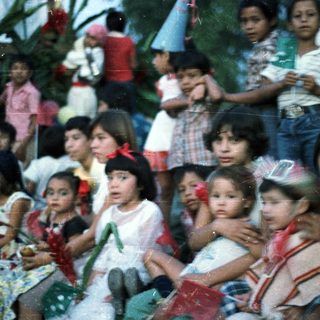 Group of children sitting together outdoors, looking toward something.