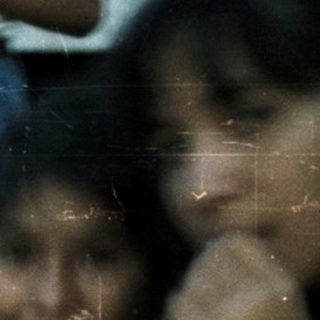 Group of children sitting together outdoors, looking toward something.