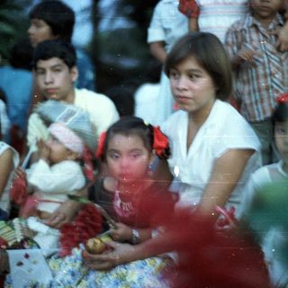 Group of children and adults gathered outdoors, appearing to watch something.