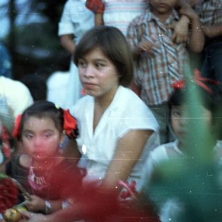Group of children and adults gathered outdoors, appearing to watch something.