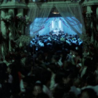 Large crowd gathers before an ornate, decorated stage.