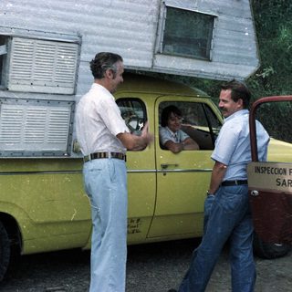 Men converse near a yellow truck with inspection signage.