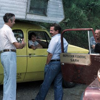 Men converse near a yellow truck with inspection signage.