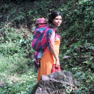 Woman carrying child, man with bag, dog on rocks.